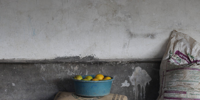 A picture of a tub of citrus fruit resting on sack against a wall.